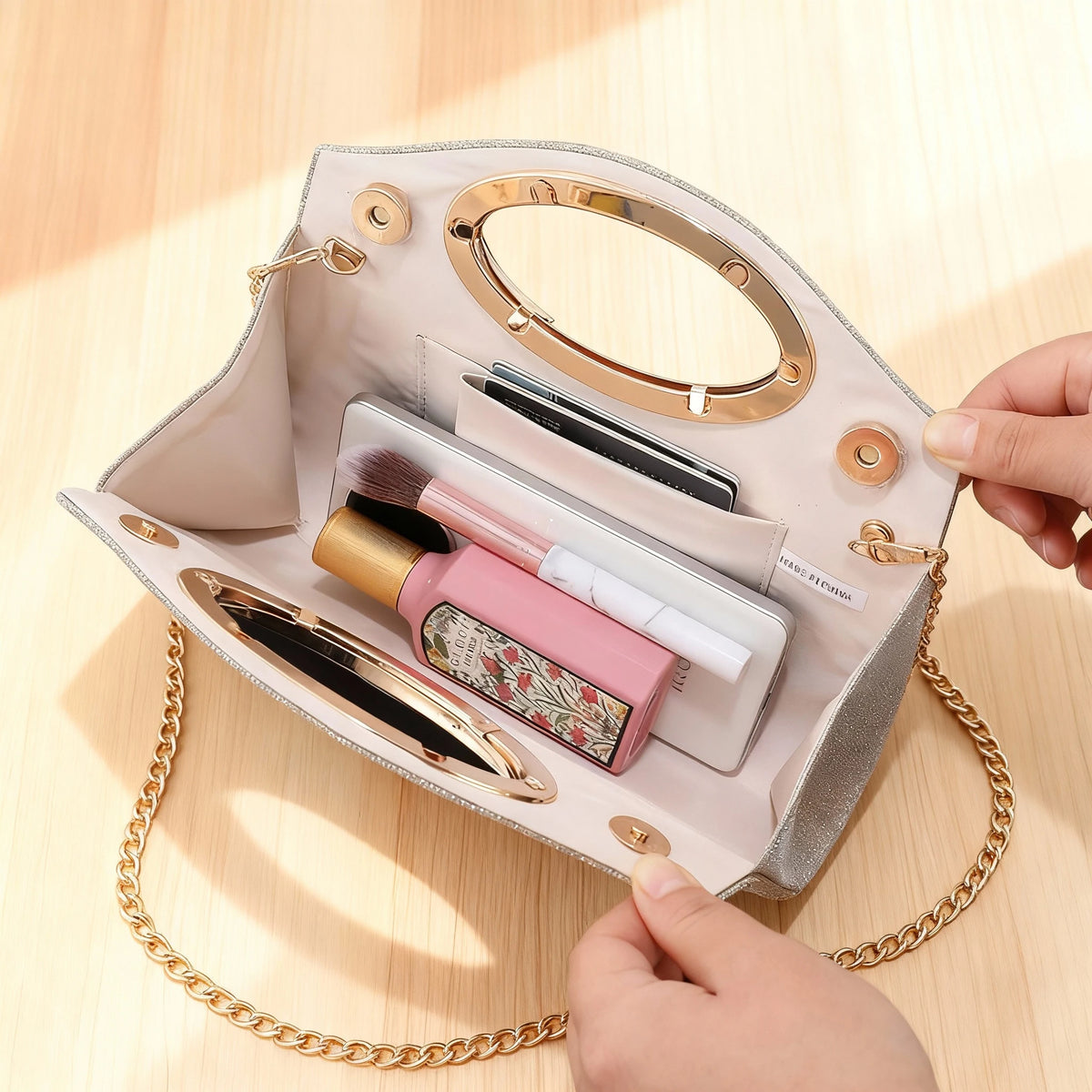 Eine hellrosa plissierte Handtasche ist geöffnet und zeigt verschiedene Make-up- und Kosmetikartikel auf einer Holzoberfläche