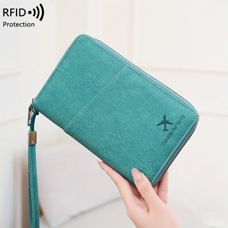 A teal leather passport wallet with a wrist strap is held by a hand, featuring an embroidered charm.