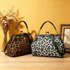 A black and brown leopard print faux leather handbag with a top handle and crossbody strap resting on a wooden surface.
