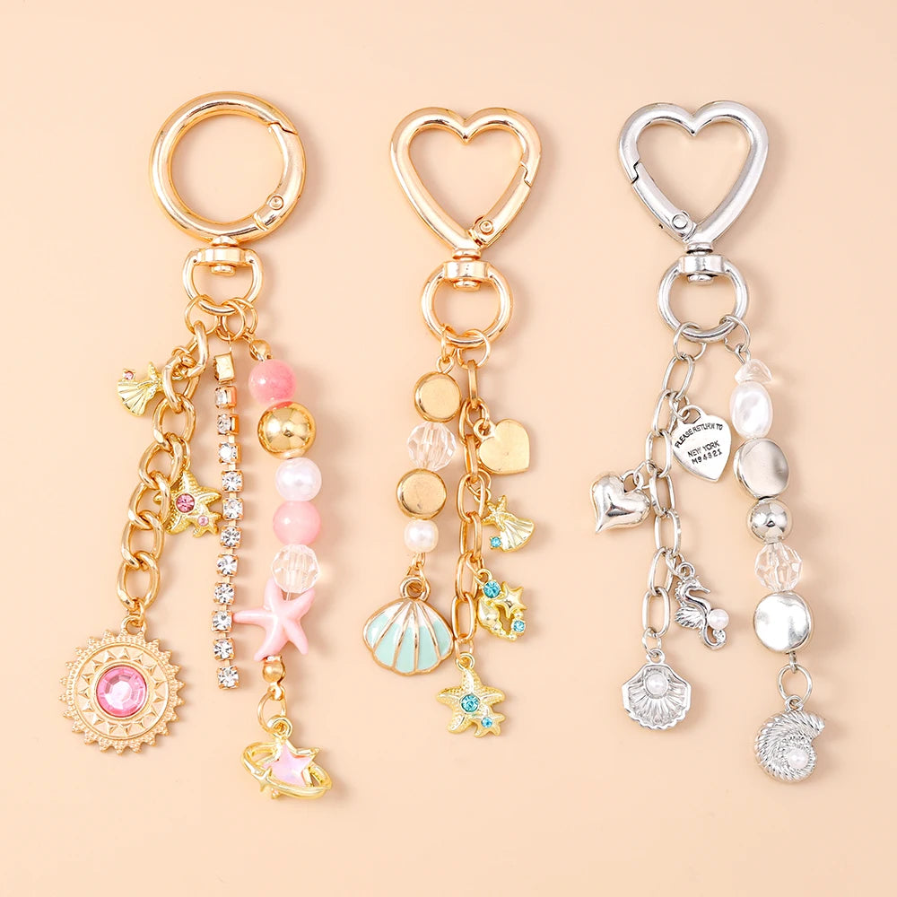 Gold and silver heart-shaped keychains featuring seashells, starfish, and pearl accents.
