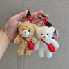 A fluffy brown teddy bear plush toy attached to a keychain with a red strap and a white bear plush toy.
