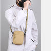 Une personne portant une veste blanche tient un sac bandoulière beige.