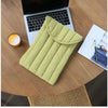 A light green embroidered cotton laptop sleeve resting on a wooden table next to a laptop and a glass.