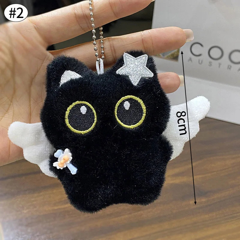 Colgante llavero de un peluche de gato negro con ojos dorados y una estrella plateada en la frente, sostenido en una mano.