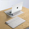 A silver laptop sleeve is shown resting on a wooden table next to an open Apple laptop.