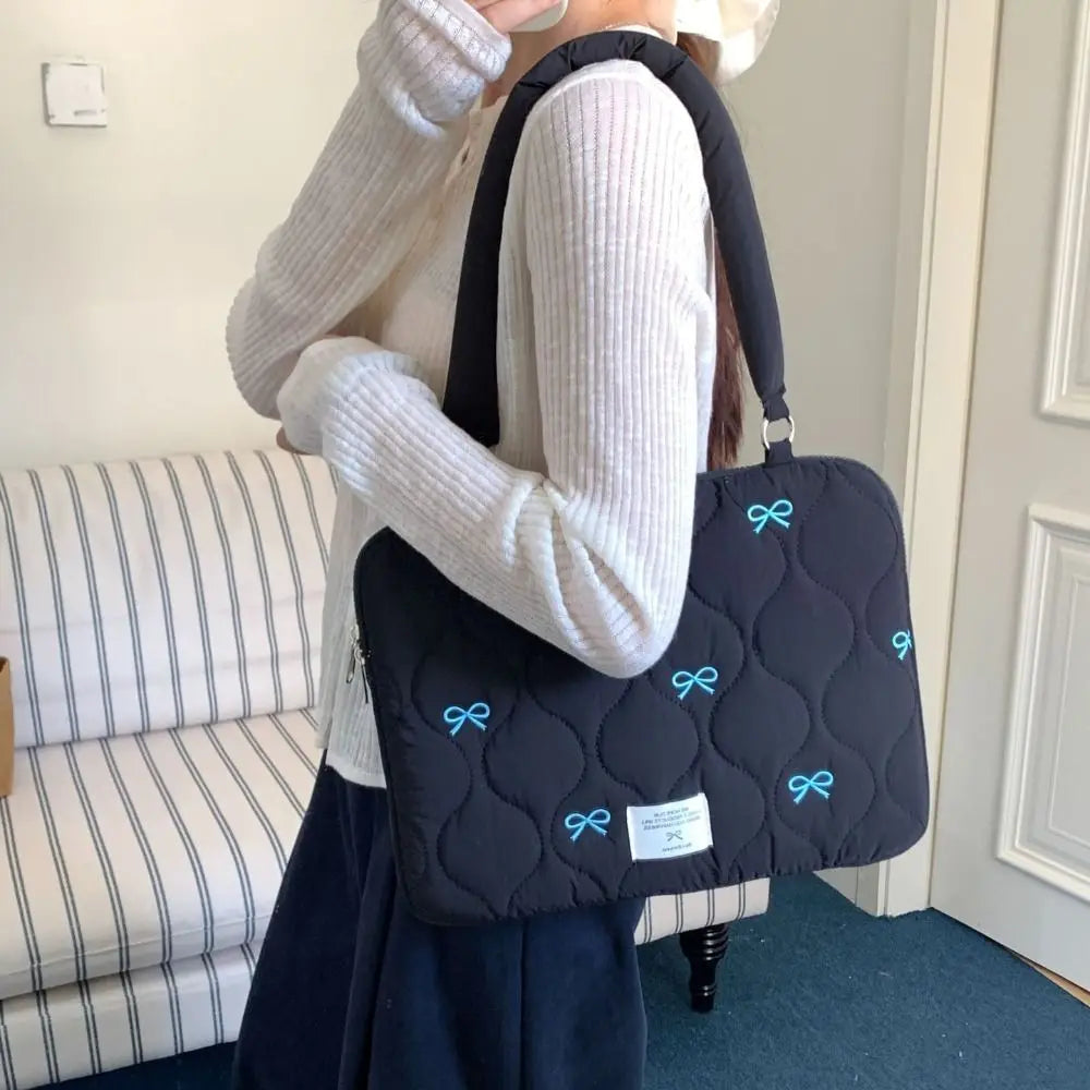 Una persona sostiene un bolso de portátil acolchado negro con detalles de lazo azul claro.
