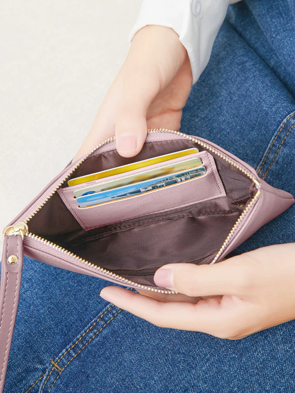 A hand is holding an open pink PU leather zipper wallet containing several credit cards and a phone.