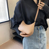 A person holds a tan PU leather shoulder bag with a strap against a dark shirt and denim jeans.
