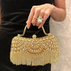 A hand holds an elegant gold and diamond rhinestone evening clutch bag with a golden tassel against a black dress.