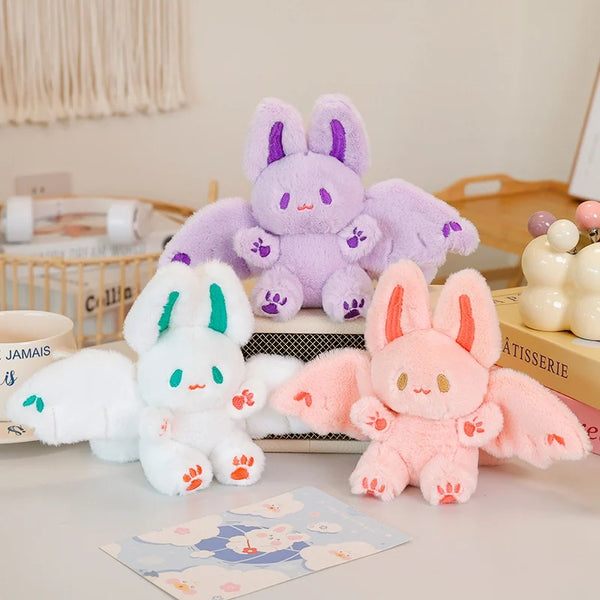 Three adorable bat bunny plush toys in purple, white, and pink colors displayed on a white surface.