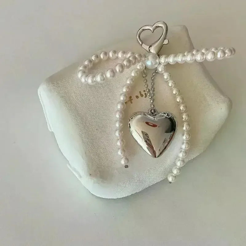 A silver pearl bow keychain featuring a heart-shaped pendant on a white background.