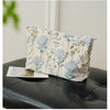 A light blue floral canvas makeup bag with gold embroidery resting on a black leather surface.