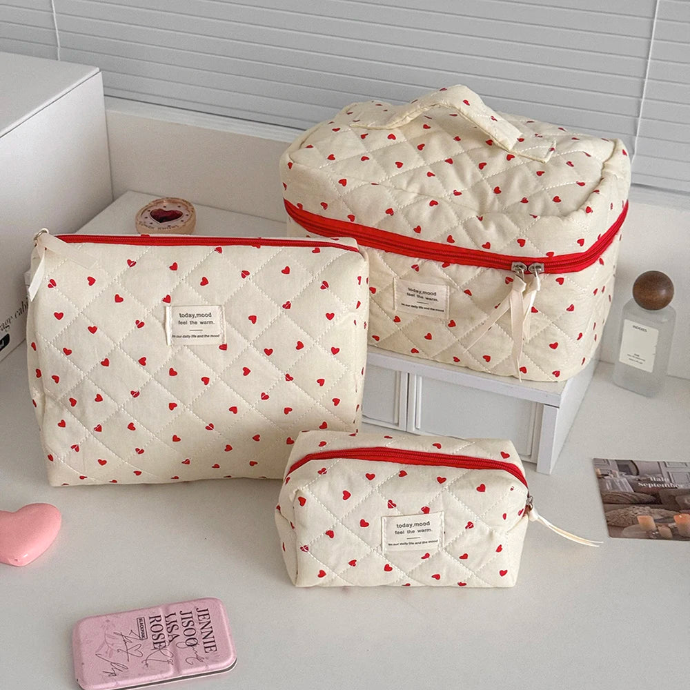 Three quilted makeup bags in cream fabric with red trim and small heart patterns are displayed on a white surface.