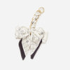 A white and black patterned fabric bow attached to a gold-toned adjustable strap for a bag or shoulder.