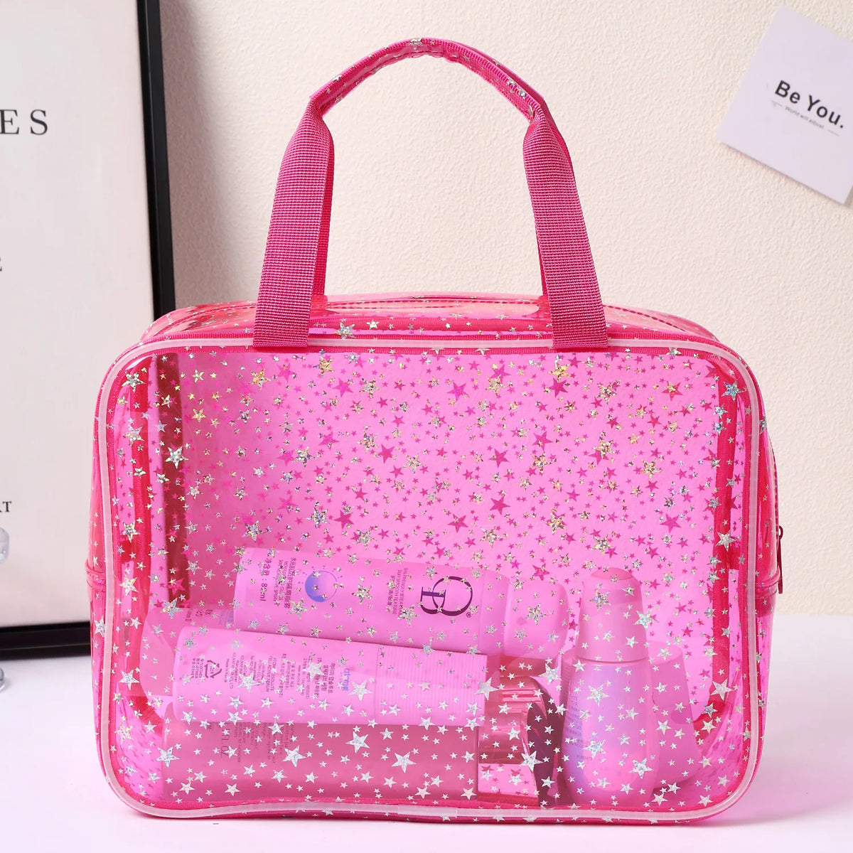 A pink clear waterproof makeup organizer bag filled with various cosmetic products and glittery stars.