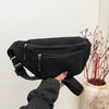 A hand holds a black corduroy crossbody waist bag with an adjustable strap against a white background.