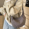 A person is holding a beige canvas crossbody shoulder bag with a gray strap and light blue jeans.