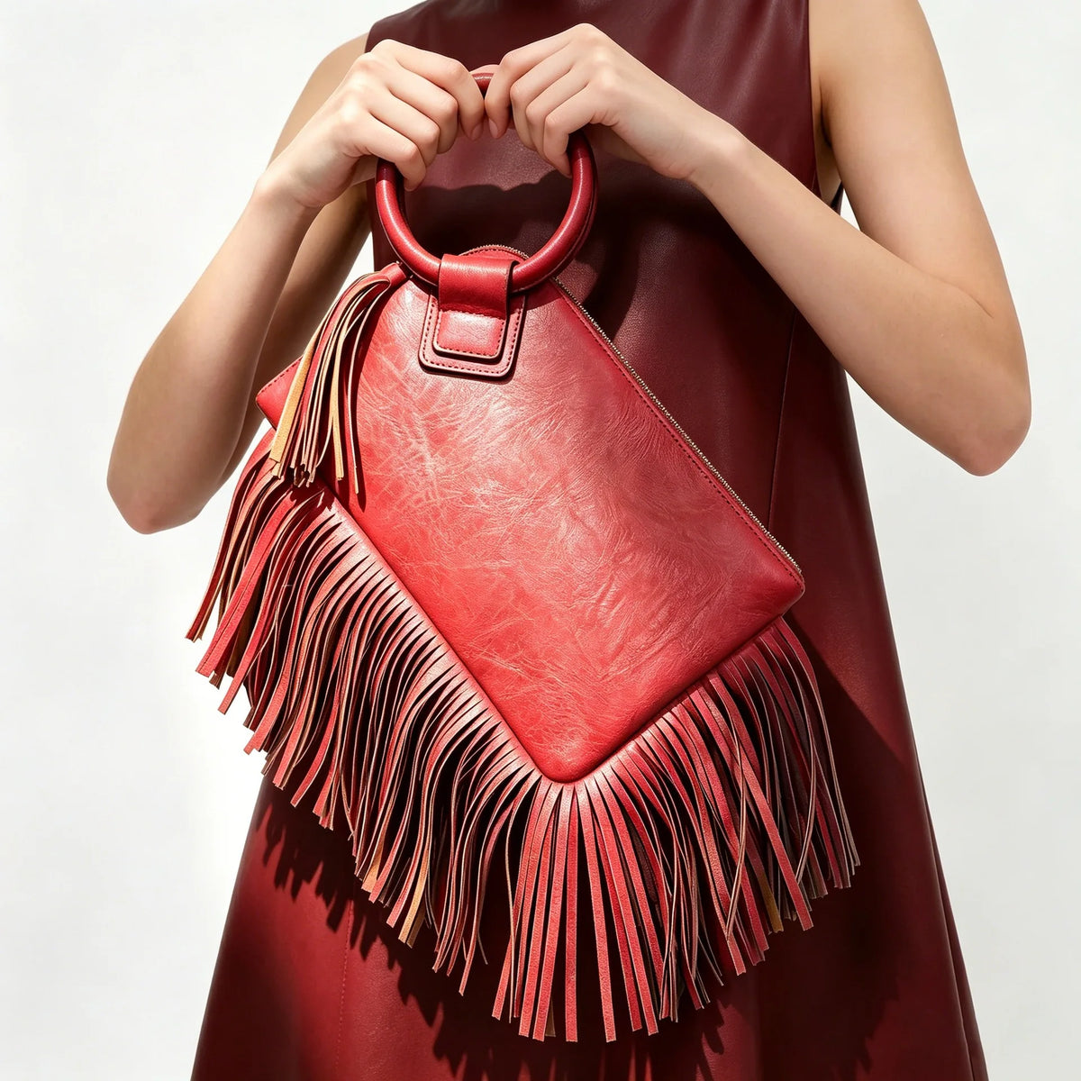 A woman holds a red leather fringed clutch bag with tassels against a light background.