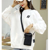 A woman wearing a white sweatshirt and light wash jeans holds a black nylon crossbody phone bag.
