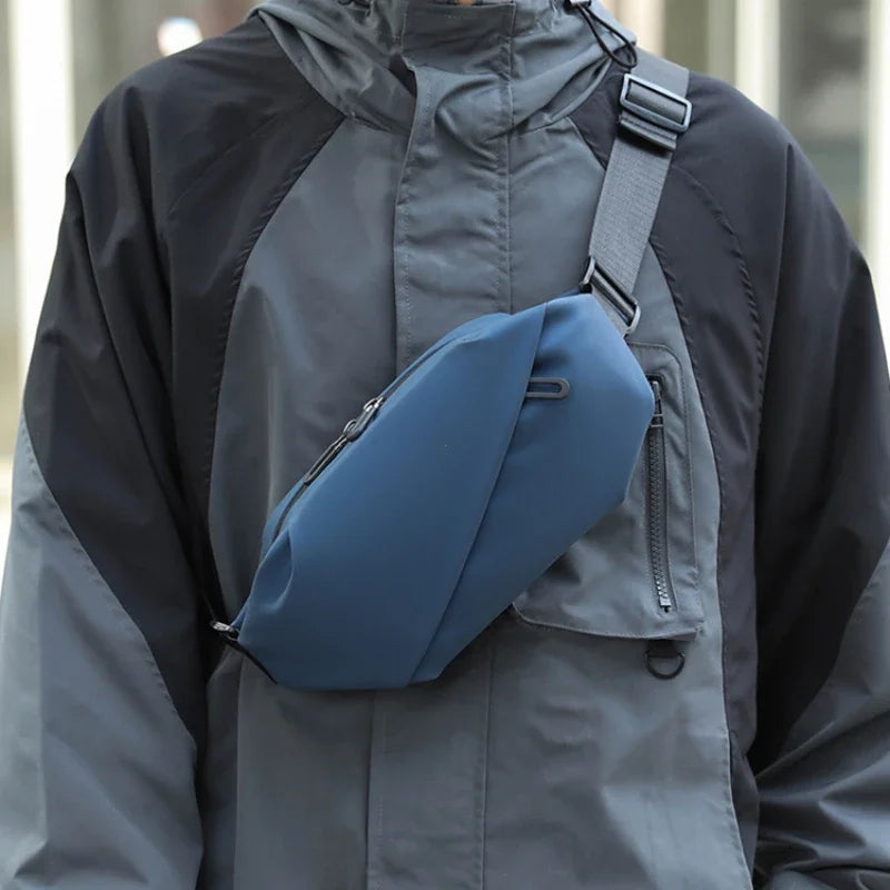 Ein Mann trägt eine graue wasserdichte Jacke mit einer schwarzen Lauftasche an der Schulter.