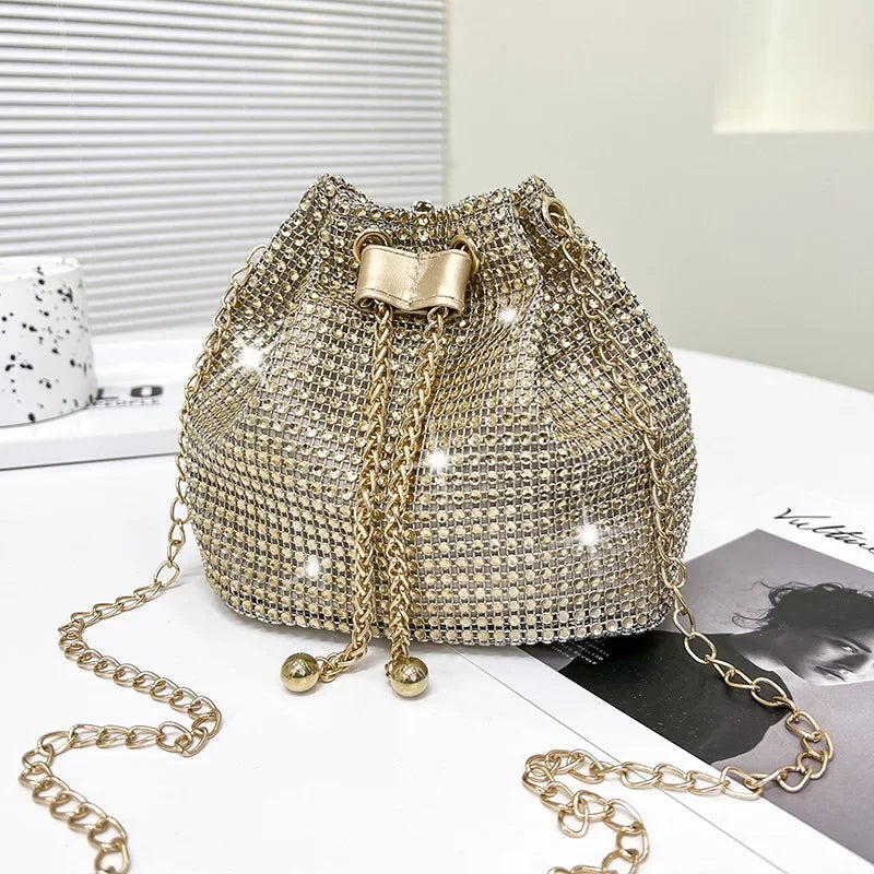 Bolso cruz con cordón y pedrería brillante dorada sobre una superficie blanca.
