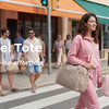 A woman carrying a pink multi-pocket travel tote bag while walking on a city sidewalk.
