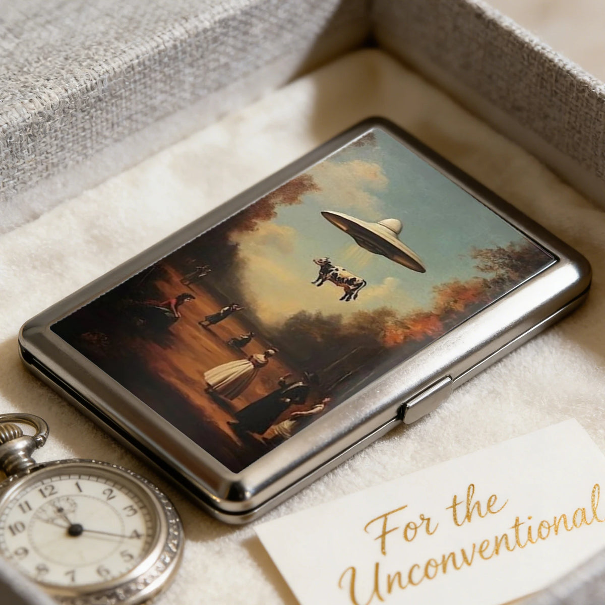 A silver metal card holder with an Art Deco design featuring a landscape painting on the cover.
