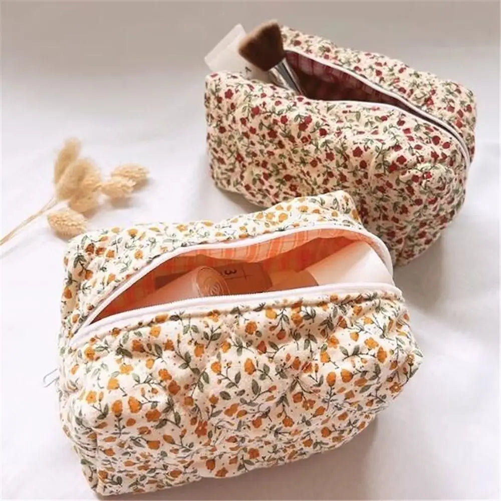 Bolsa de maquillaje acolchada con cremallera floral en patrones crema y naranja, sobre una superficie blanca.