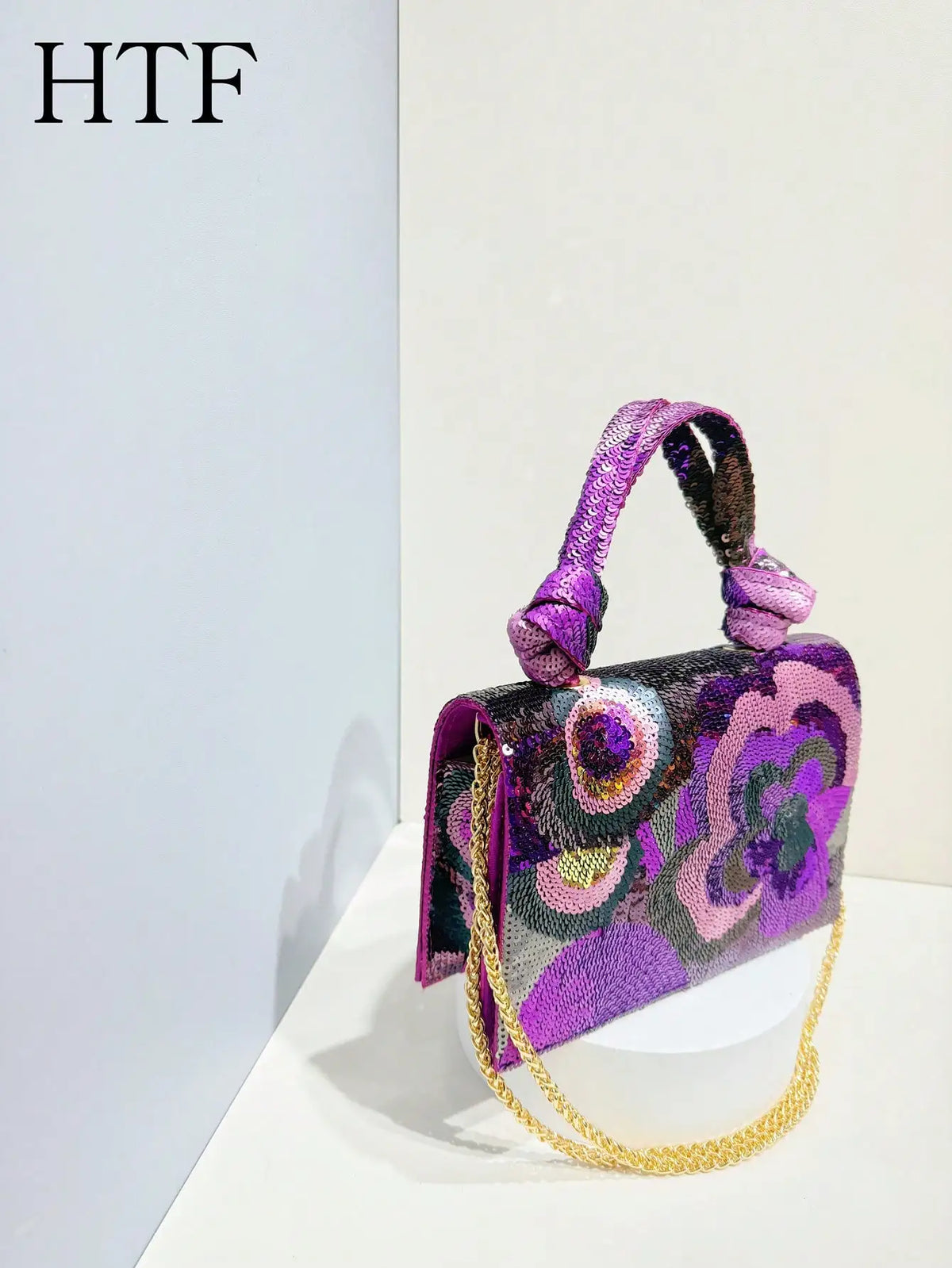 A purple sequin embroidered floral clutch bag with a purple strap displayed against a white background.