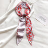 Foulard de soie floral rose et blanc noué en nœud, exposé sur fond de tissu blanc.