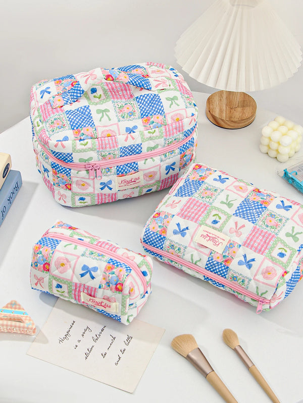 A pink and blue patchwork quilted makeup bag resting on a white surface next to a wooden object and makeup brushes.