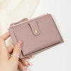 A hand holds a light pink ultra-thin PU leather card holder wallet with a stitched flap and gold hardware.