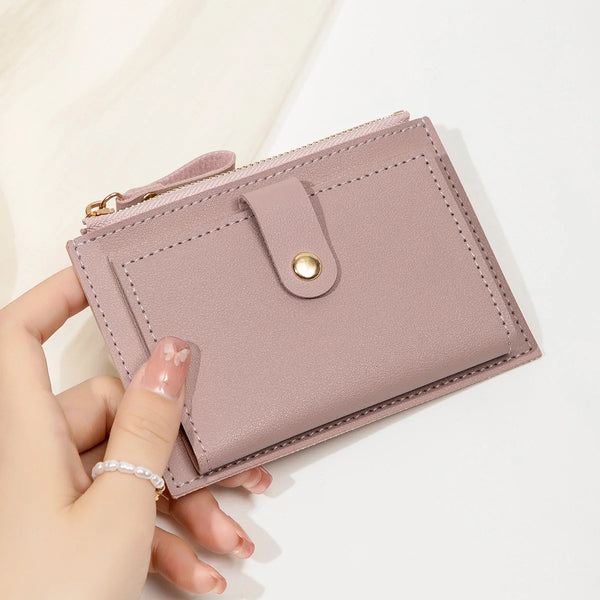A hand holds a light pink ultra-thin PU leather card holder wallet with a stitched flap and gold hardware.