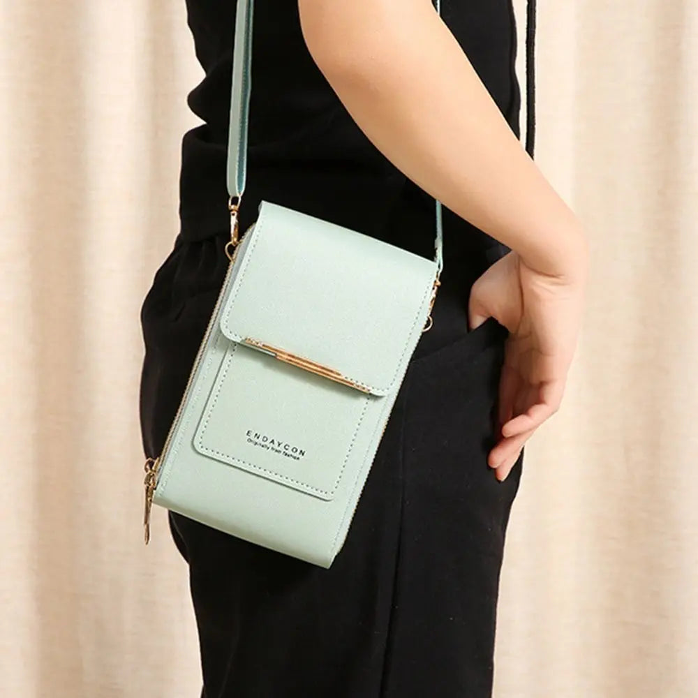 A light mint green RFID-protected touch screen crossbody bag with gold hardware being held by a person.