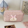 A pink quilted cosmetic storage pouch with a white lace bow resting on a white surface.