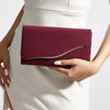 A woman holds a deep burgundy velvet evening clutch with a silver trim against a white dress.