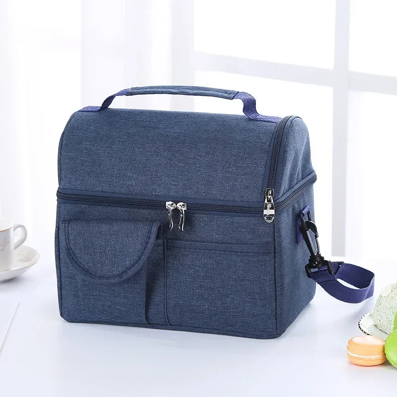 A dark blue reusable insulated lunch bag with a handle and front pocket resting on a white surface.
