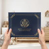 A person holds an elegant dark blue birth certificate holder with gold detailing and an eagle emblem.