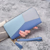 A light blue and gray checkered fashion zipper wallet is held by a hand on a gray surface.