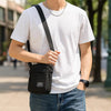 A man wearing a white t-shirt and jeans carrying a black compact crossbody sling bag.