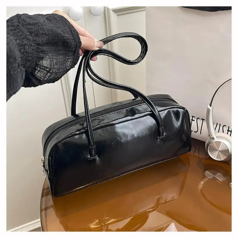 A black glossy PU leather tote bag with dual straps resting on a wooden surface.