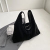 A black suede slouchy shoulder bag resting on a white surface next to a gray blazer.