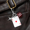 Llavero de plata con dije de dados rojo y negro, sujeto a una correa de bolso de cuero marrón.