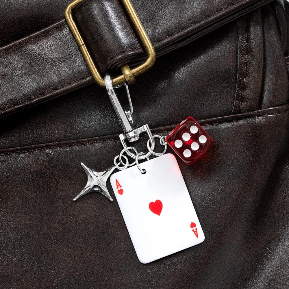 Llavero de plata con dije de dados rojo y negro, sujeto a una correa de bolso de cuero marrón.