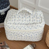 A light blue floral patterned quilted cosmetic bag sitting on a wooden surface.