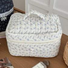 Sac de maquillage rembourré à motif floral bleu clair sur une surface en bois.