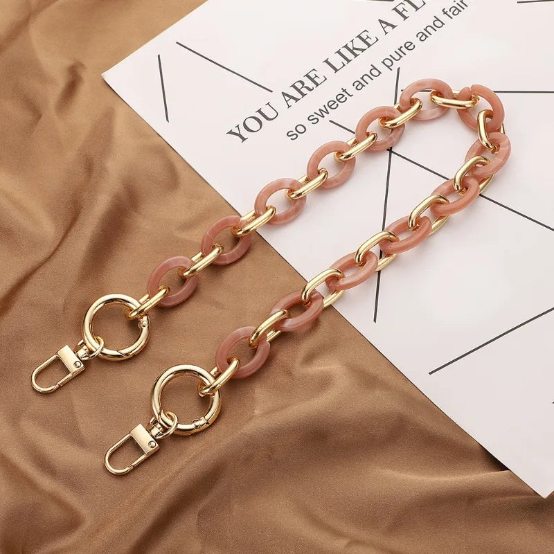 Une paire de breloques à chaîne en acrylique or et rose posées sur un tissu marron à côté d'un papier.
