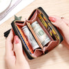 A hand holds an open compact PU leather tassel wallet with a zipper closure displaying rolled US dollar bills.