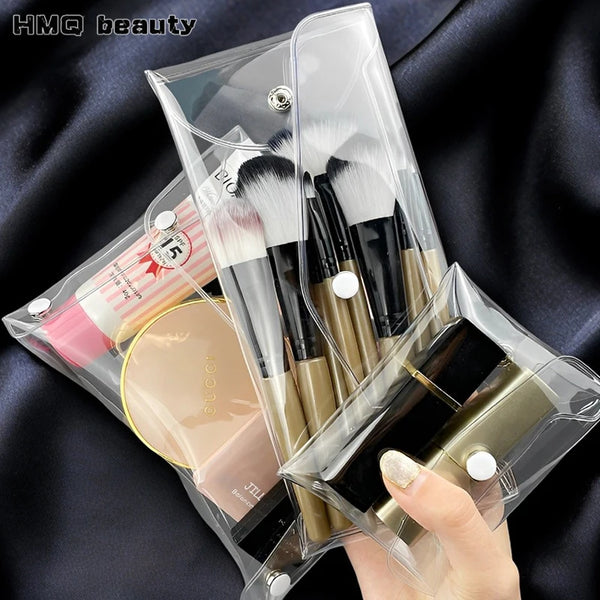 A hand holds a clear plastic pouch containing various makeup brushes and cosmetic tools.