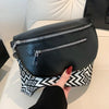 A black PU leather multi-pocket crossbody bag with silver zippers is held by a hand against a white surface.